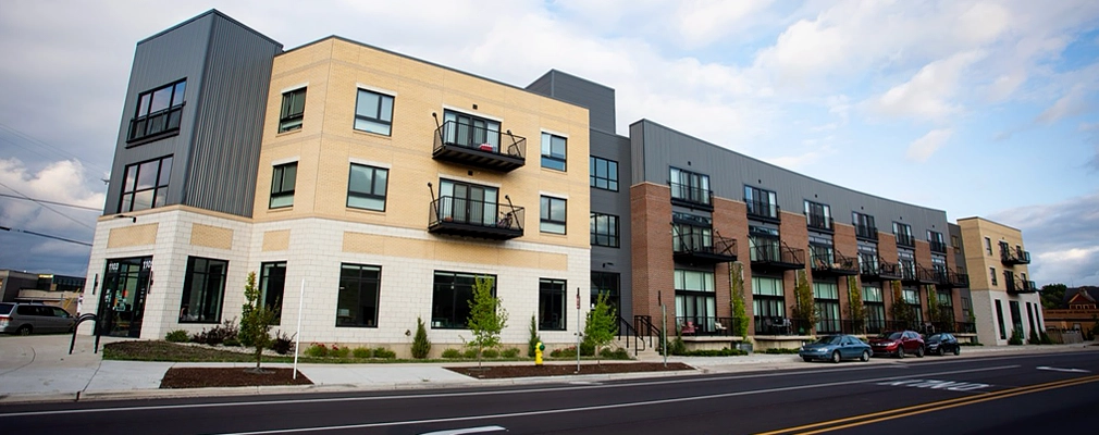 Exterior view of the Creamery Apartments in Kalamazoo, Michigan — a modern mixed-use HUD-subsidized housing development with balconies and street-level retail.
